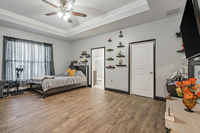 bedroom with connected bathroom, a raised ceiling, hardwood / wood-style floors, ornamental molding, and ceiling fan