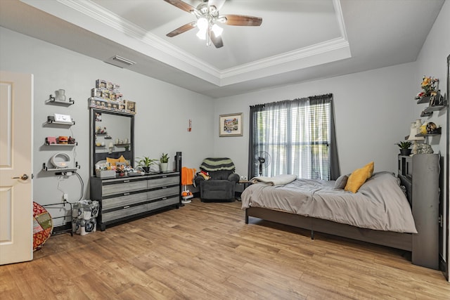 bedroom with light wood-type flooring, a raised ceiling, crown molding, and ceiling fan