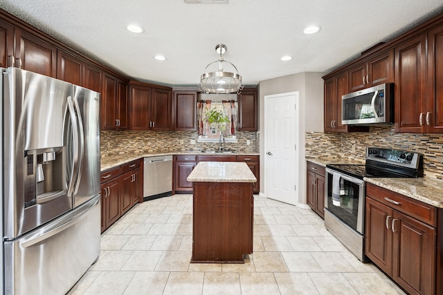 kitchen with appliances with stainless steel finishes, a kitchen island, light stone countertops, sink, and a notable chandelier