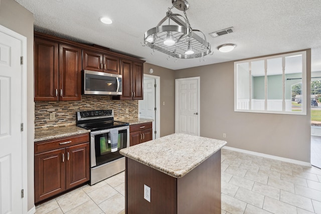 kitchen featuring a chandelier, a textured ceiling, a center island, tasteful backsplash, and appliances with stainless steel finishes