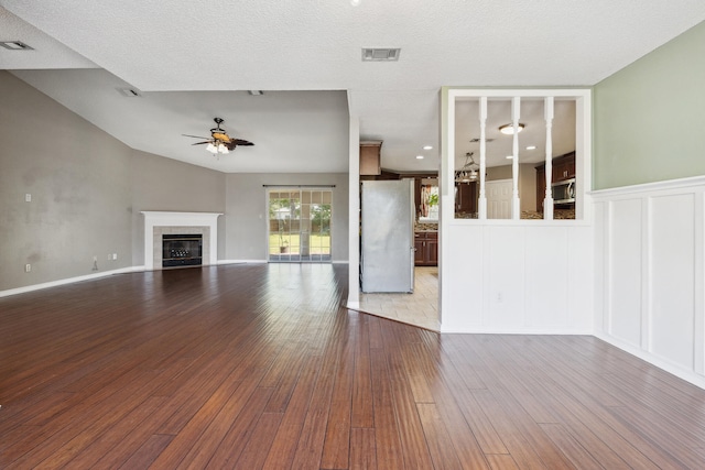 unfurnished living room with a textured ceiling, hardwood / wood-style flooring, lofted ceiling, a tiled fireplace, and ceiling fan