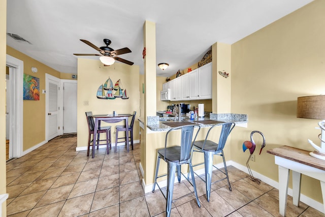 kitchen with kitchen peninsula, stainless steel range with electric stovetop, ceiling fan, white cabinets, and a breakfast bar area