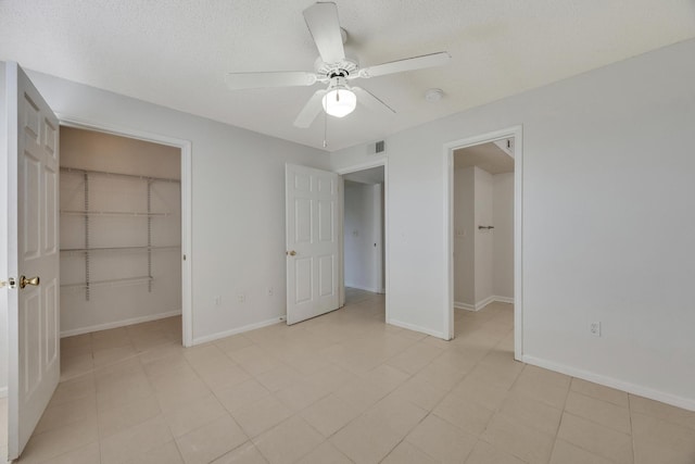 unfurnished bedroom with a textured ceiling, a spacious closet, ceiling fan, and a closet