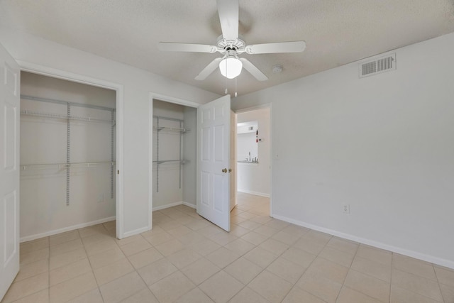 unfurnished bedroom with a textured ceiling, light tile patterned floors, ceiling fan, and multiple closets