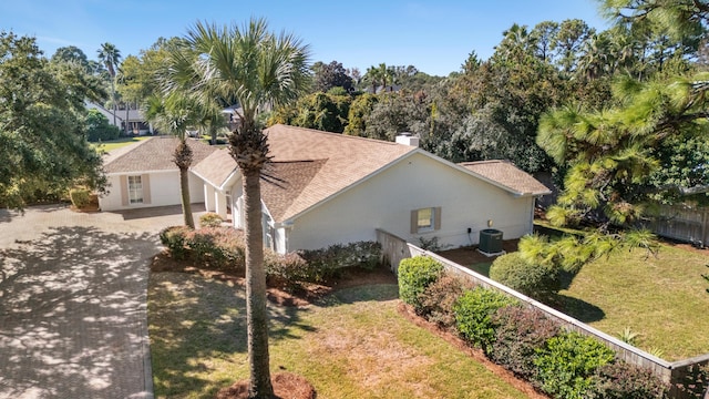 view of side of home featuring fence, a lawn, driveway, and central AC unit