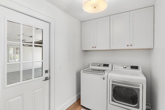 clothes washing area featuring washing machine and dryer, baseboards, cabinet space, and wood finished floors