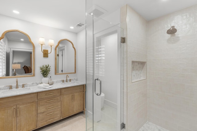 bathroom with double vanity, a shower stall, visible vents, and a sink