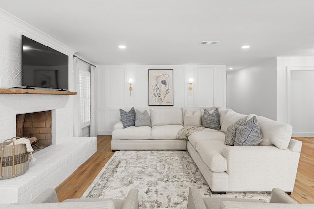 living area with a fireplace, a decorative wall, wood finished floors, and visible vents
