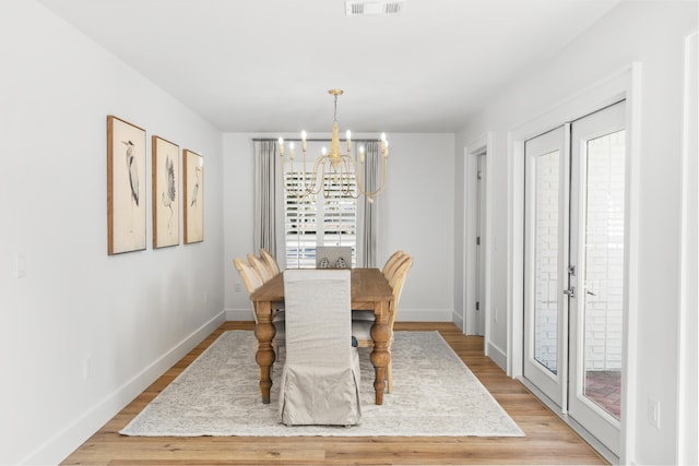 dining space featuring an inviting chandelier, french doors, and light wood-type flooring