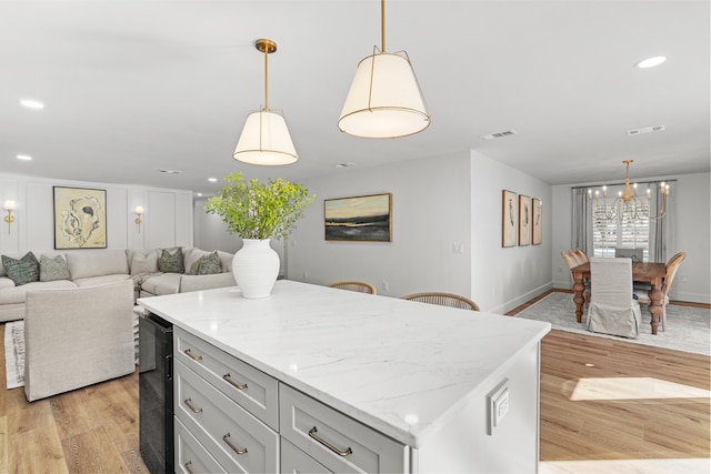 kitchen with light hardwood / wood-style flooring, a center island, light stone counters, and pendant lighting