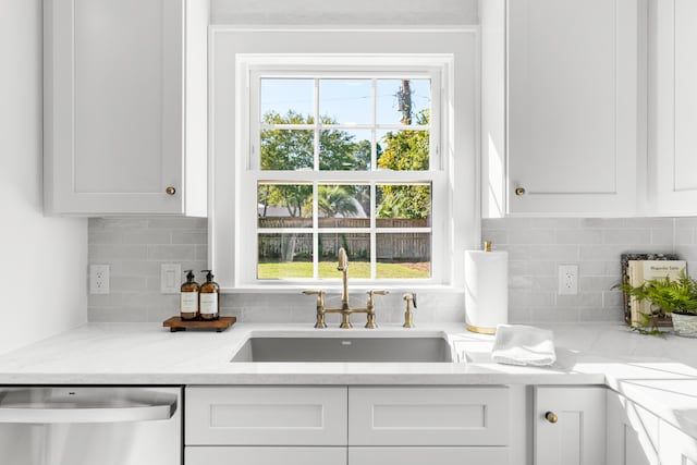 kitchen with white cabinets, light stone countertops, stainless steel dishwasher, and sink