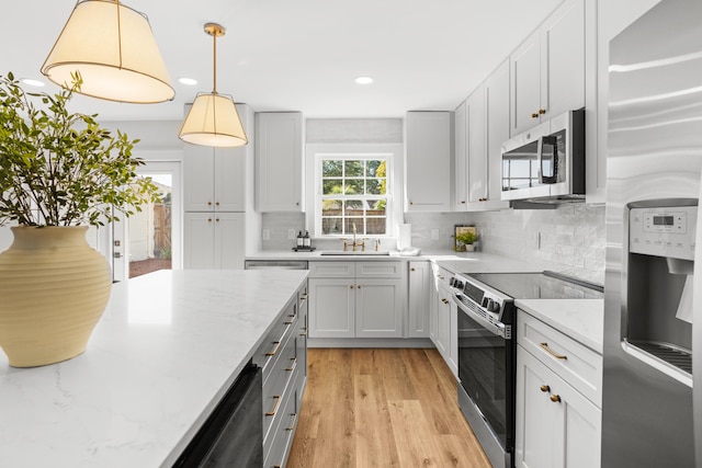 kitchen featuring appliances with stainless steel finishes, sink, light hardwood / wood-style floors, pendant lighting, and light stone counters