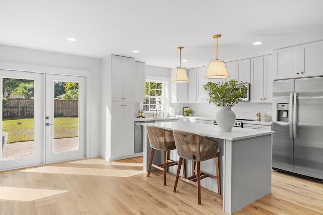 kitchen with a kitchen island, a breakfast bar, light wood-type flooring, stainless steel appliances, and decorative light fixtures