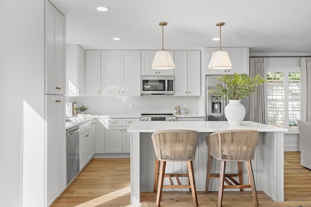 kitchen featuring a kitchen island, stainless steel appliances, pendant lighting, light wood-type flooring, and white cabinetry