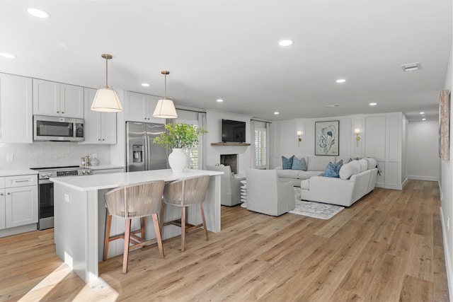 kitchen with appliances with stainless steel finishes, light hardwood / wood-style flooring, a fireplace, and white cabinets