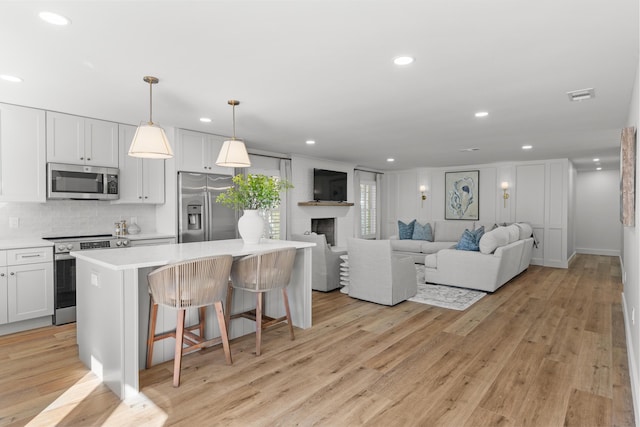 living area featuring recessed lighting, light wood-style flooring, visible vents, and a large fireplace