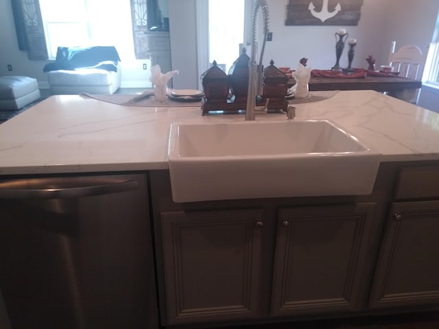 kitchen featuring light stone countertops, stainless steel dishwasher, sink, and a wealth of natural light