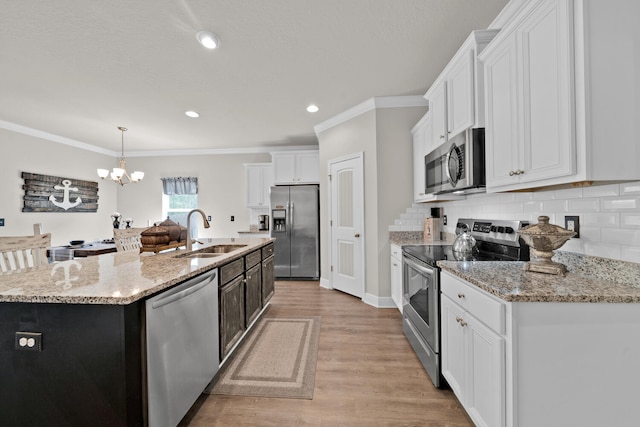 kitchen with appliances with stainless steel finishes, white cabinets, pendant lighting, a kitchen island with sink, and sink