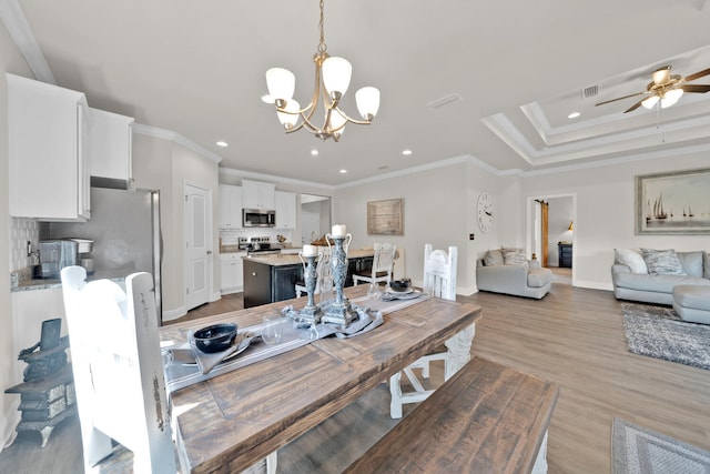 dining room featuring light wood-type flooring, ceiling fan with notable chandelier, ornamental molding, and a raised ceiling