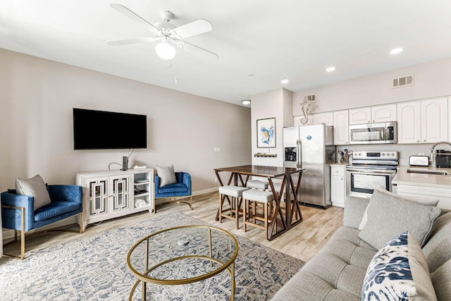 living room with light wood-type flooring, ceiling fan, and sink