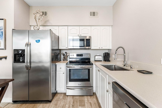 kitchen featuring a sink, light countertops, light wood finished floors, stainless steel appliances, and white cabinetry