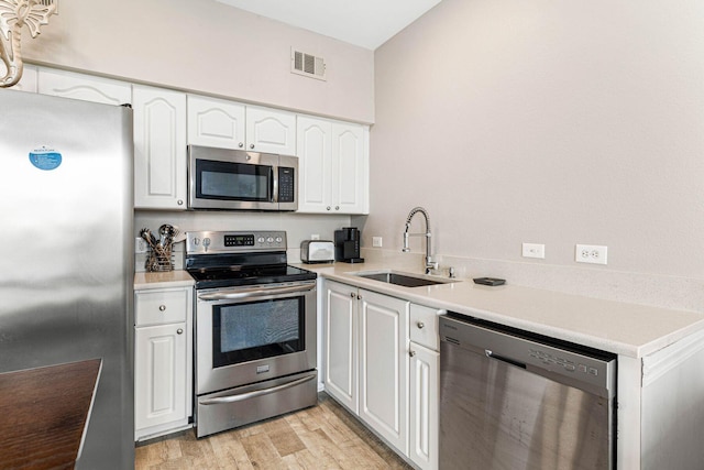 kitchen featuring visible vents, appliances with stainless steel finishes, a sink, white cabinets, and light wood finished floors