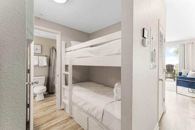 bedroom with light wood-style floors, ensuite bath, and access to exterior
