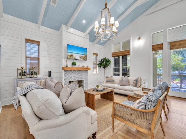 living room featuring beam ceiling, a tiled fireplace, an inviting chandelier, high vaulted ceiling, and light hardwood / wood-style flooring