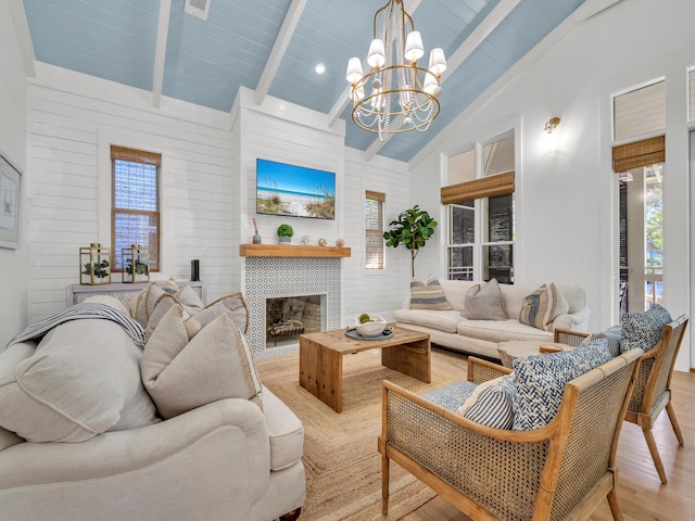 living room featuring light wood-type flooring, a tiled fireplace, beam ceiling, high vaulted ceiling, and a chandelier