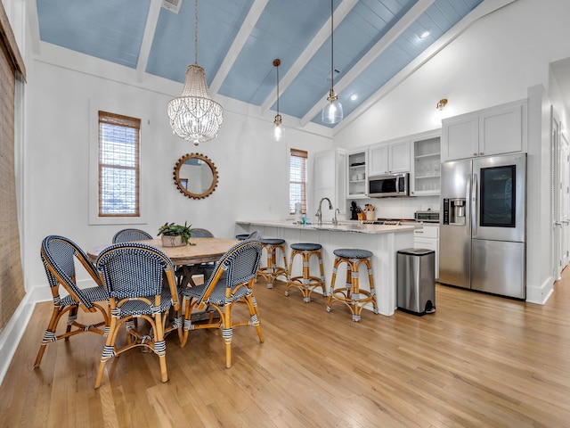 dining space featuring beam ceiling, an inviting chandelier, high vaulted ceiling, light hardwood / wood-style floors, and sink