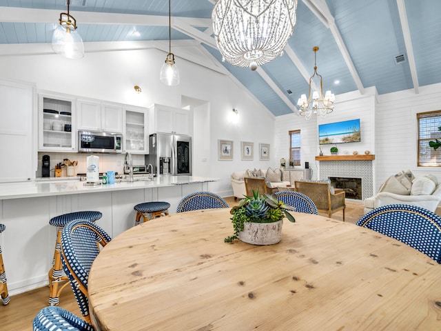 dining space featuring sink, a fireplace, beam ceiling, high vaulted ceiling, and a chandelier