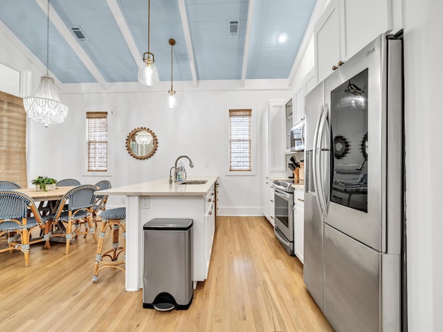 kitchen with sink, stainless steel appliances, pendant lighting, white cabinets, and a kitchen island with sink