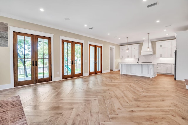 unfurnished living room with light parquet flooring, crown molding, and french doors