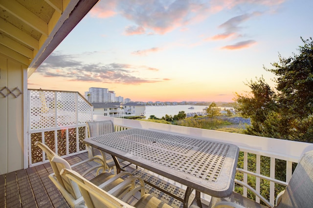 balcony at dusk featuring a deck with water view