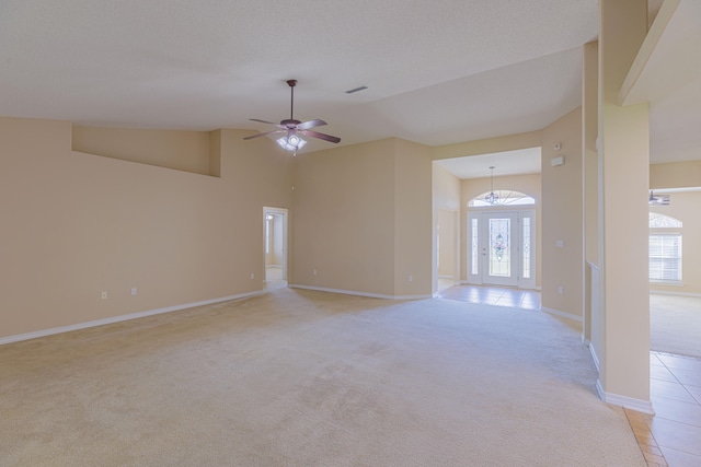 carpeted empty room with ceiling fan with notable chandelier, high vaulted ceiling, a healthy amount of sunlight, and french doors