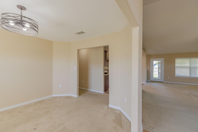 carpeted spare room featuring an inviting chandelier and a textured ceiling