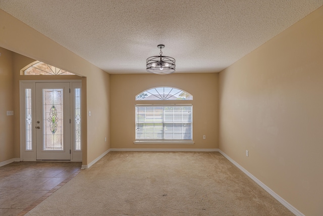 carpeted foyer with a notable chandelier and a textured ceiling