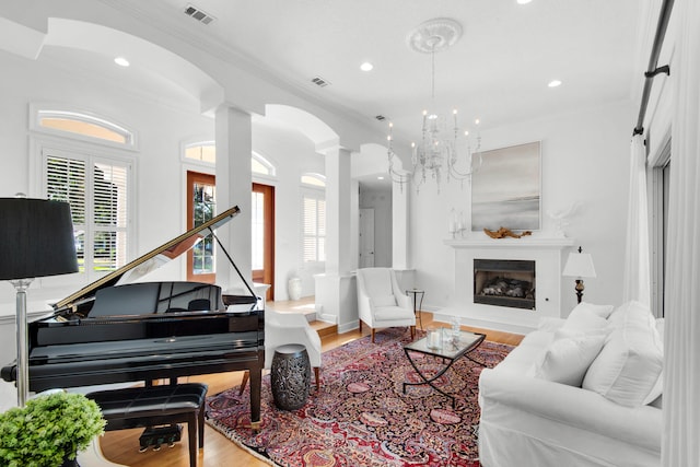 living room featuring ornamental molding, light hardwood / wood-style floors, an inviting chandelier, and ornate columns