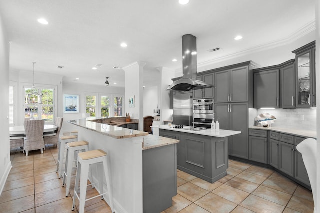 kitchen featuring pendant lighting, island exhaust hood, a center island with sink, and gray cabinetry