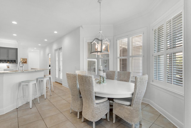 dining space featuring a notable chandelier, light tile patterned flooring, crown molding, and sink