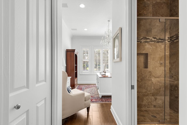 corridor with wood-type flooring, crown molding, and a chandelier