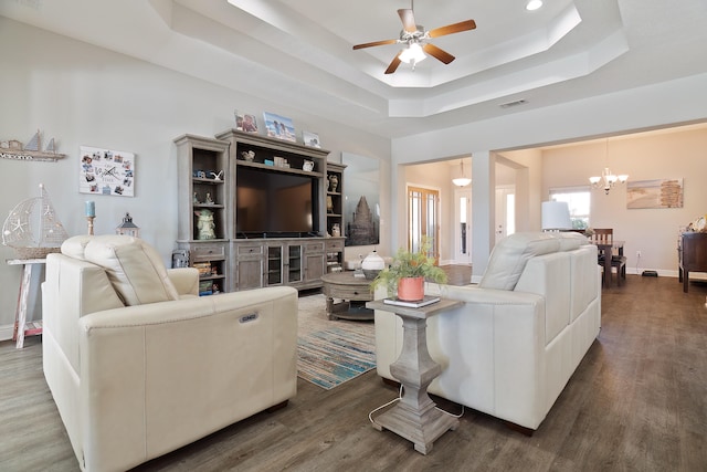 living room featuring dark wood-type flooring, ceiling fan with notable chandelier, and a raised ceiling