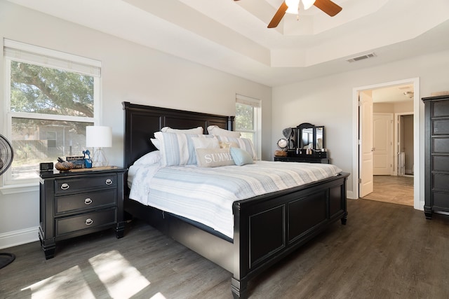 bedroom with dark hardwood / wood-style floors, a tray ceiling, and ceiling fan