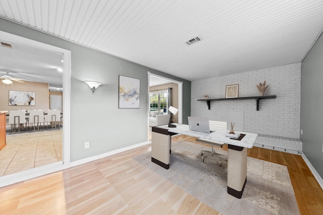 office area with brick wall, light wood-type flooring, and ceiling fan