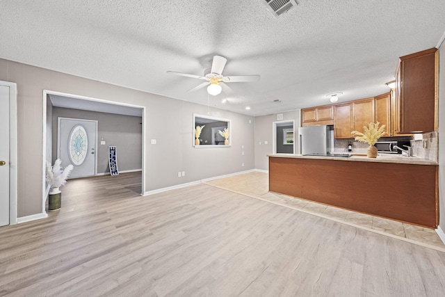 kitchen featuring kitchen peninsula, light hardwood / wood-style flooring, decorative backsplash, ceiling fan, and stainless steel fridge