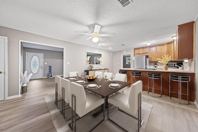 dining space with ceiling fan, a textured ceiling, and light hardwood / wood-style floors