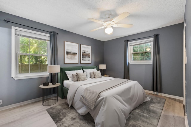 bedroom with light wood-type flooring, multiple windows, ceiling fan, and a textured ceiling