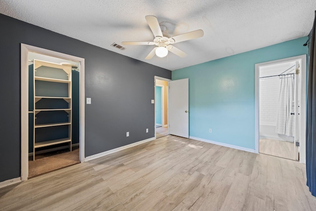 unfurnished bedroom with light hardwood / wood-style floors, a textured ceiling, a walk in closet, ensuite bathroom, and ceiling fan