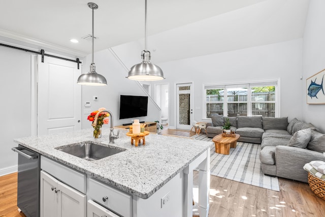 kitchen featuring light hardwood / wood-style floors, an island with sink, a barn door, decorative light fixtures, and sink