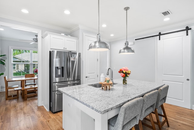 kitchen featuring light wood-type flooring, white cabinets, stainless steel refrigerator with ice dispenser, a barn door, and light stone countertops